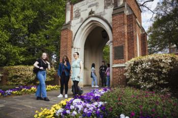students walking near campus building with flowers